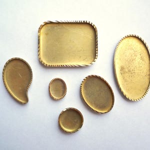 May include: Six gold-colored metal trays of various shapes and sizes. The trays have a decorative, textured edge.