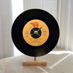 May include: A black vinyl record clock with gold hands and a white label. The label features a red and orange illustration of a bull with the text "RSO" and "SO 515". The record is titled "Nights on Broadway" by "Bee Gees".
