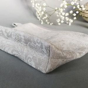 May include: A white zippered pouch with a floral pattern. The pouch is made of a soft, textured fabric and has a zipper closure.