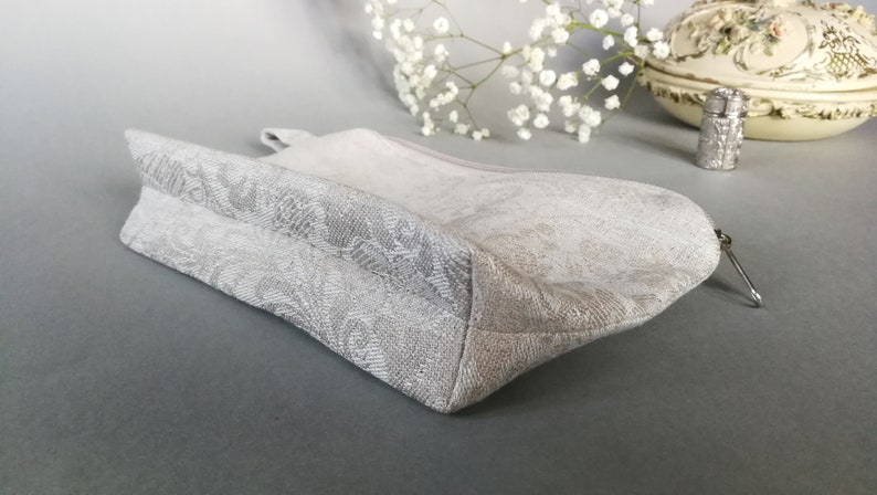 May include: A white zippered pouch with a floral pattern. The pouch is made of a soft, textured fabric and has a zipper closure.