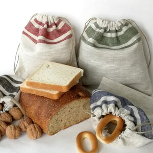 Op de afbeelding: Een assortiment vers brood, bagels en walnoten wordt getoond met linnen zakken met trekkoord. De zakken hebben rode, groene en blauwe strepen. Het brood is gesneden en klaar om te eten.