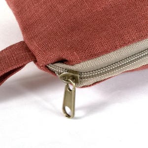 May include: A close-up of a red zippered pouch with a brown fabric strap. The zipper is made of metal and has a silver finish.
