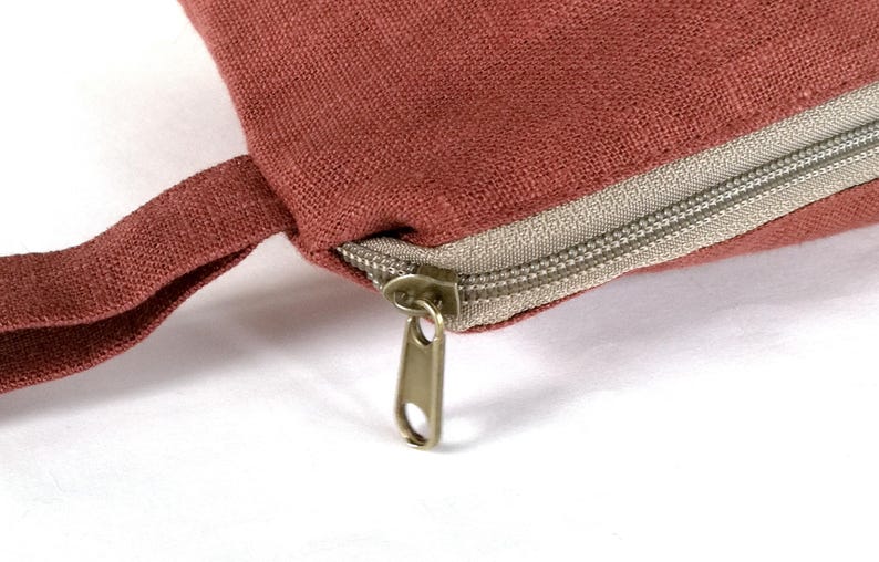 May include: A close-up of a red zippered pouch with a brown fabric strap. The zipper is made of metal and has a silver finish.