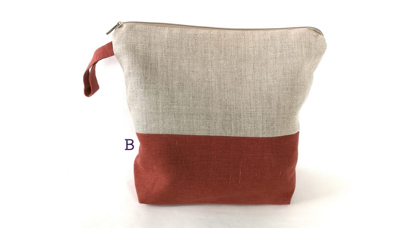 May include: A large zippered pouch made of linen fabric. The top half of the pouch is a light beige color, and the bottom half is a deep reddish-brown color.