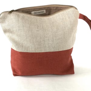 May include: A beige and rust-colored linen zippered pouch with a top handle. The pouch has the text "OneFrontLinen" printed on the inside.