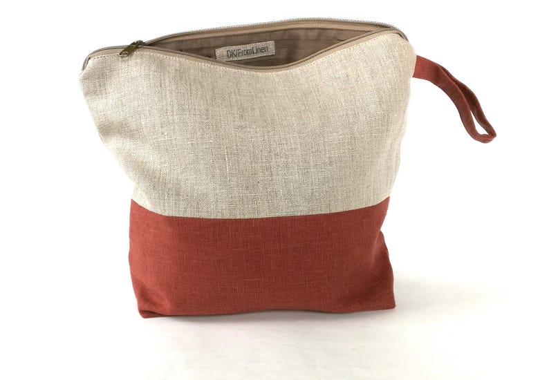 May include: A beige and rust-colored linen zippered pouch with a top handle. The pouch has the text "OneFrontLinen" printed on the inside.