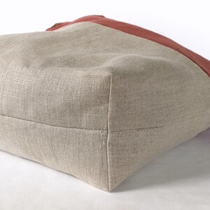 May include: A beige linen tote bag with a red linen panel on the top. The bag is shown from the bottom, with the seams visible.