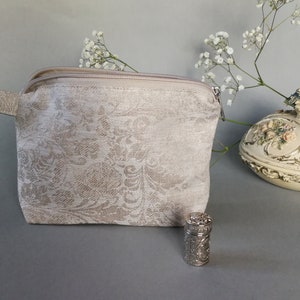 May include: A beige zippered pouch with a floral pattern. The pouch has a small handle and is made of a soft fabric.