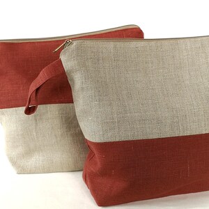 May include: Two linen tote bags with a red and natural linen color scheme. The bags have a zipper closure and a top handle.