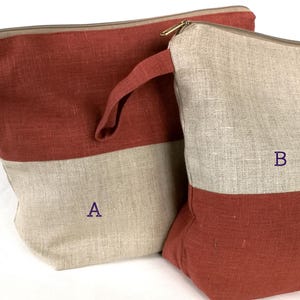 May include: Two linen zippered pouches, one red and beige, the other beige and red. The larger pouch has a handle and is labeled "A". The smaller pouch is labeled "B".