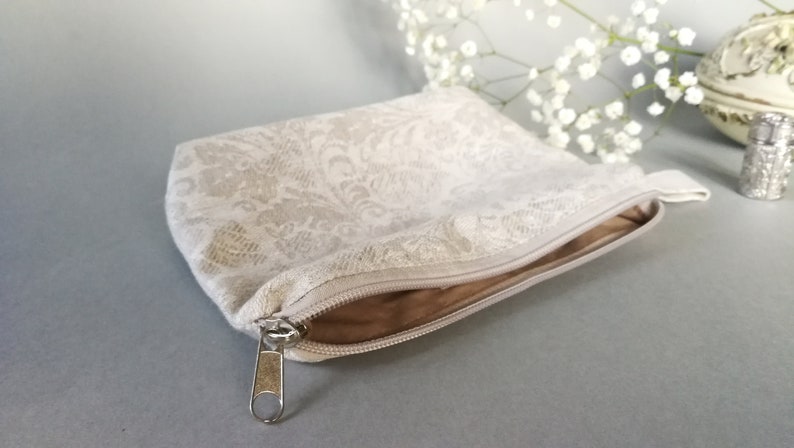 May include: A white zippered pouch with a delicate floral pattern. The pouch is made of a soft, textured fabric and has a silver zipper.