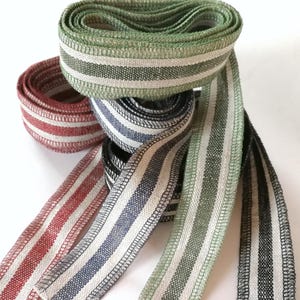 May include: Four rolls of striped fabric ribbon in red, blue, green, and black. The ribbon is woven with white stripes.