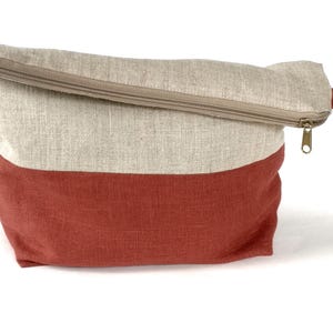 May include: A beige and red linen zippered pouch with a handle. The pouch is made of a natural fabric and has a simple design.