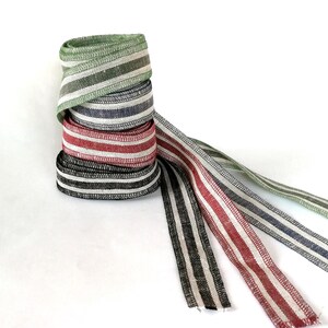 May include: Four rolls of striped ribbon in green, blue, red, and black. The ribbon is woven with white stripes.