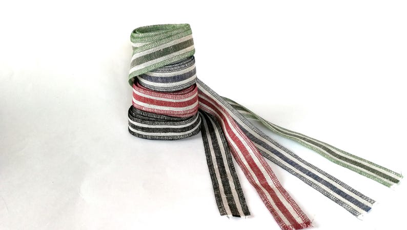 May include: Four rolls of striped ribbon in green, blue, red, and black. The ribbon is woven with white stripes.
