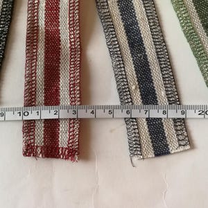 May include: Four different striped fabric ribbons with white and a contrasting color. The ribbons are measured with a ruler in inches. The colors are black, red, blue, and green.