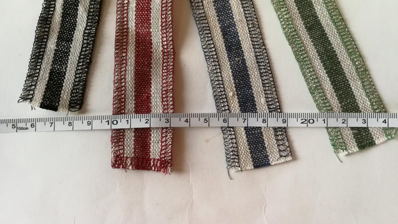 May include: Four different striped fabric ribbons with white and a contrasting color. The ribbons are measured with a ruler in inches. The colors are black, red, blue, and green.