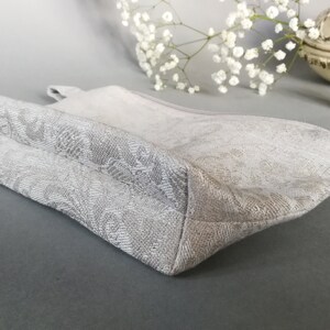 May include: A white zippered pouch with a floral pattern. The pouch is made of a soft, textured fabric and has a zipper closure.