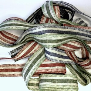 May include: A collection of striped ribbon in red, green, and blue colors. The ribbon is woven with a linen texture.