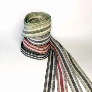 May include: A stack of four striped ribbons in green, white, black, and red. The ribbons are rolled up and tied together with a long, flowing tail.