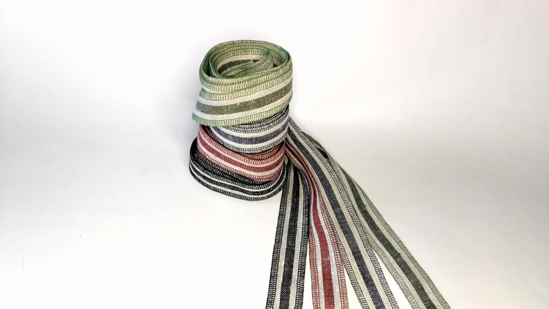 May include: A stack of four striped ribbons in green, white, black, and red. The ribbons are rolled up and tied together with a long, flowing tail.