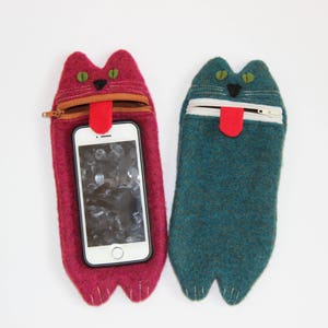 Puede incluir: Dos fundas para tel&eacute;fono de fieltro con forma de gato, una roja y otra azul turquesa, con una cremallera y una lengua de fieltro que sobresale. Ambas fundas tienen un tel&eacute;fono blanco en su interior.