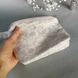 May include: A white zippered pouch with a floral pattern. The pouch has a white fabric handle.