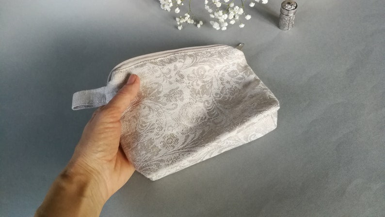 May include: A white zippered pouch with a floral pattern. The pouch has a white fabric handle.