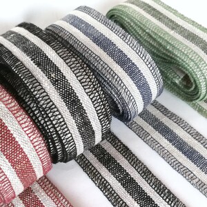 May include: Five different striped fabric ribbons in red, black, gray, green, and white. The ribbons are woven with a textured pattern and have a subtle sheen.
