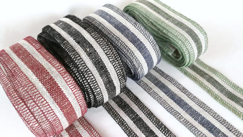 May include: Five different striped fabric ribbons in red, black, gray, green, and white. The ribbons are woven with a textured pattern and have a subtle sheen.