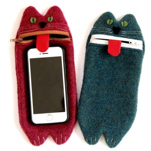 Puede incluir: Dos fundas para tel&eacute;fono de fieltro con forma de gato con la boca abierta y la lengua fuera. La funda de la izquierda es roja y la funda de la derecha es azul.