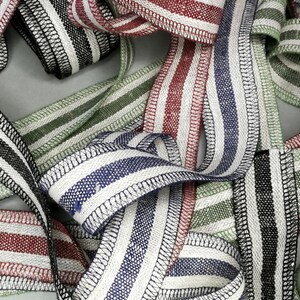 May include: A collection of striped fabric ribbon with different color combinations, including black and white, red and white, green and white, and blue and white. The ribbon is woven with a textured finish and has a stitched edge.