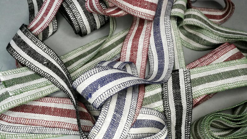 May include: A collection of striped fabric ribbon with different color combinations, including black and white, red and white, green and white, and blue and white. The ribbon is woven with a textured finish and has a stitched edge.