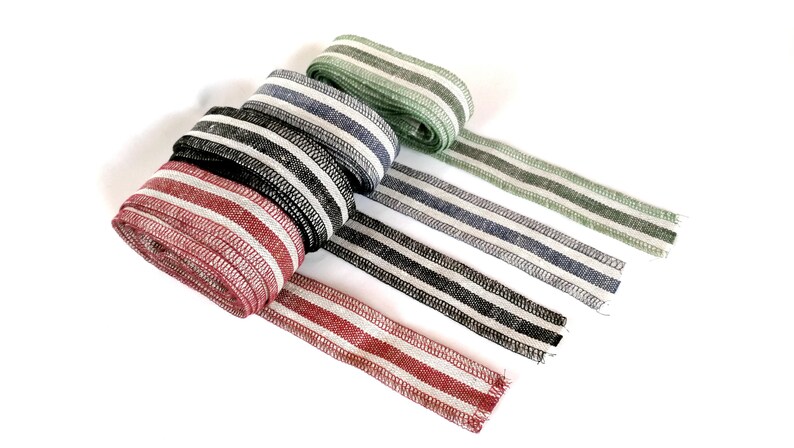 May include: Four rolls of striped fabric ribbon in red, black, blue, and green. The ribbon is woven with white stripes.