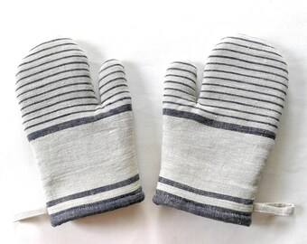 Puede incluir: Un par de guantes de cocina con un patrón de rayas grises y blancas. Los guantes tienen un lazo para colgar y están diseñados para proteger las manos del calor al cocinar. El diseño general es simple y funcional.