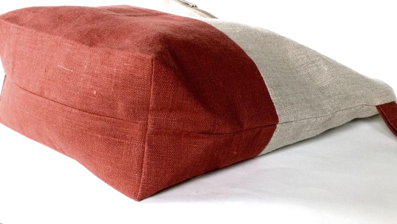 May include: A red and beige linen tote bag with a contrasting color block design. The bag is made of a soft, natural fabric and has a simple, understated style.