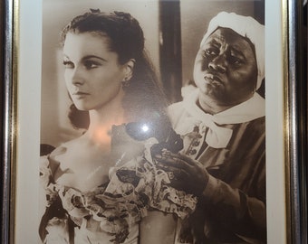 May include: Black and white framed photograph featuring two women. One woman is in a period dress, and the other is wearing a white head covering. The photograph is in a silver and gold frame.