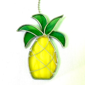 May include: A stained glass pineapple suncatcher with a yellow pineapple and green leaves. The pineapple has a silver wire design.