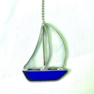 Könnte beinhalten: Ein Bleiglas-Sonnenfänger in Form eines Segelboots mit blauem Rumpf und klaren Segeln, der an einer silbernen Kette hängt.