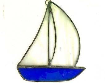 May include: A stained glass sailboat ornament with a blue hull and white sails. The ornament is made of glass and metal and has a rustic look.