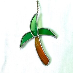Peut inclure: Une décoration en verre coloré en forme de palmier avec des feuilles vertes et un tronc orange. La décoration est suspendue à une chaîne argentée.