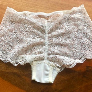May include: White lace underwear with a scalloped edge. The underwear has a floral pattern and is made of a sheer fabric.