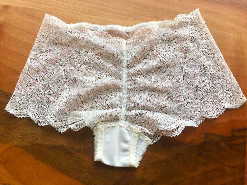 May include: White lace underwear with a scalloped edge. The underwear has a floral pattern and is made of a sheer fabric.