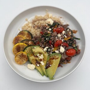May include: A white bowl filled with a meal of brown rice, ground beef, spinach, tomatoes, zucchini, avocado, and feta cheese.