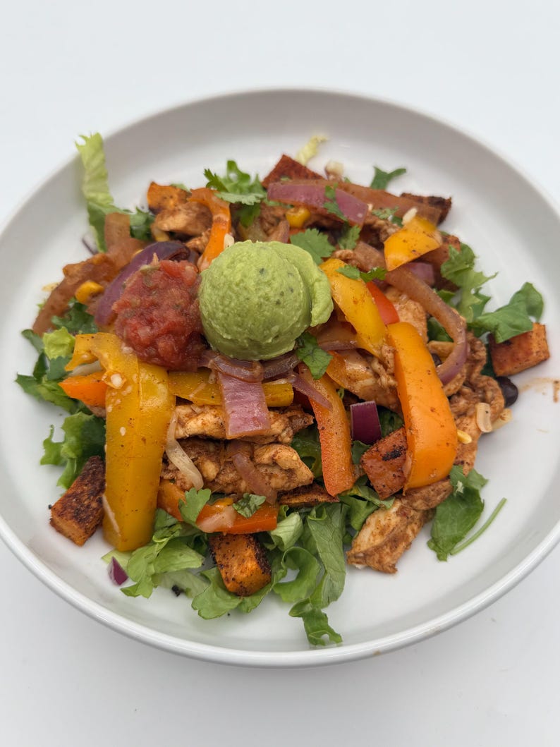 May include: A white bowl filled with a colorful salad featuring chicken, peppers, onions, sweet potatoes, and a dollop of guacamole.