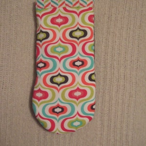 May include: A white fabric pouch with a geometric pattern in shades of red, green, blue, and black. The pouch has a white trim around the top edge.