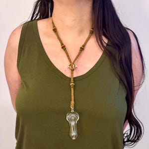 May include: A brown leather cord necklace with green beads and a clear glass pipe pendant. The pipe is shaped like a teardrop and has a small hole at the top for smoking.