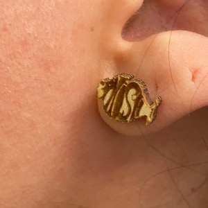 May include: A pair of gold-colored fish-shaped earrings with the word "FISH" written on them.