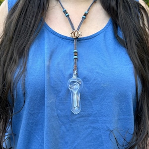 May include: A clear glass pipe hangs from a blue and brown beaded necklace. The necklace has a wooden pendant with the word "MOSH" carved into it.