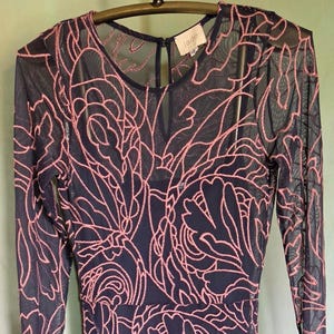 May include: A navy blue dress with a pink floral design and long sleeves. The dress has a sheer overlay, a round neckline, and a flowing skirt. The label reads "jade".